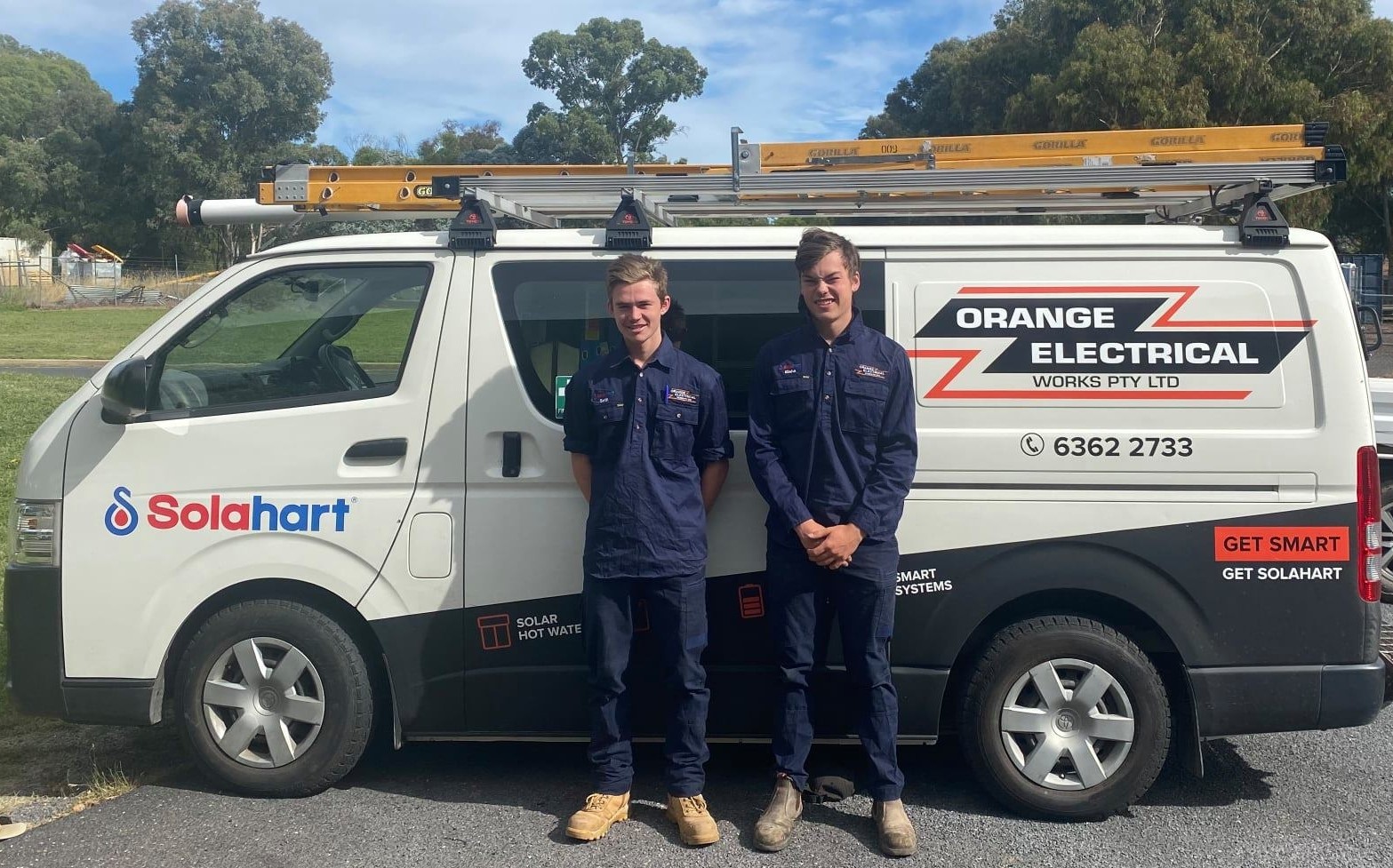 Two apprentices from Orange Electrical Works standing in front of a Toyota Hiace van